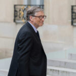 A man in a suit walking outdoors with a slight smile