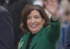 Liquor Law Drama: Hochul’s Olympic Exception A smiling woman in a green coat waving at an outdoor event