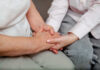An older persons hand being held by a younger persons hand, symbolizing care and connection