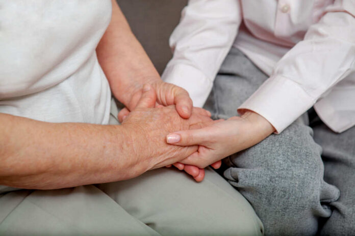 An older persons hand being held by a younger persons hand, symbolizing care and connection