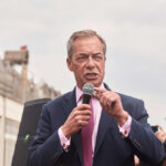 A man in a suit speaking into a microphone at an outdoor rally