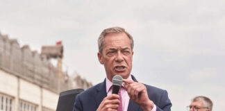 A man in a suit speaking into a microphone at an outdoor rally