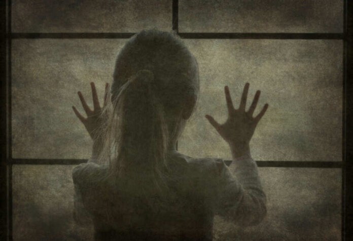 Silhouette of a child with hands pressed against a window, looking outside