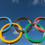 Five interlocking Olympic rings against a blue sky with clouds