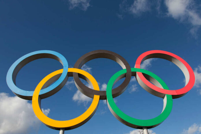 Five interlocking Olympic rings against a blue sky with clouds