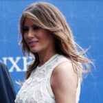 Melania’s STUNNING Entrance Shakes Up Congress A woman with long hair wearing an elegant white dress, smiling at an outdoor event