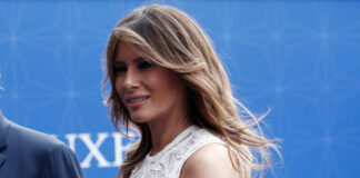 A woman with long hair wearing an elegant white dress, smiling at an outdoor event