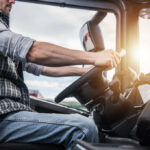 A truck driver gripping the steering wheel inside a vehicle cabin