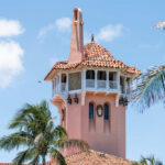 A pink tower with a tiled roof surrounded by palm trees against a blue sky