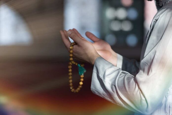 Person holding prayer beads with hands raised