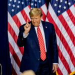 Democrats ERUPT During Trump SOTU A man in a suit gesturing with one finger in front of multiple American flags