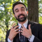 Man in business attire speaking outdoors with a natural background