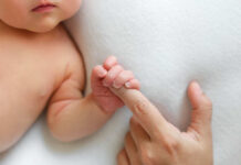A close-up of a babys hand grasping an adult finger