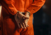 Individual in an orange jumpsuit with hands cuffed behind their back