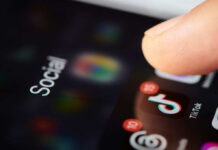 Close-up of a finger tapping a TikTok icon on a smartphone screen with social media labels