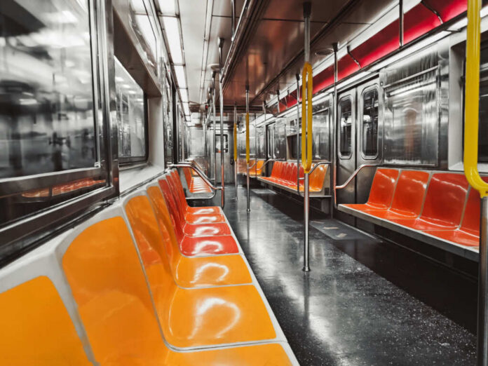 Interior of an empty subway train with orange seats and metallic surfaces