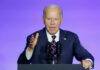 A man in a suit speaking at a podium with microphones against a blue background