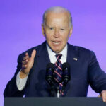 A man in a suit speaking at a podium with microphones against a blue background