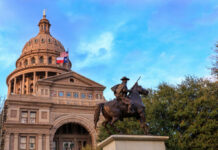 Statue of a rider in front of the Texas State Capitol building under a blue sky