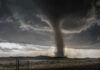 A tornado forming under dark storm clouds in a rural landscape