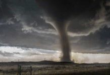 A tornado forming under dark storm clouds in a rural landscape