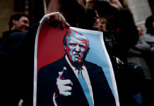 A person holding a protest sign featuring a stylized illustration of a man with a serious expression