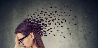 A woman with glasses holding her head, with fragments dispersing from her head