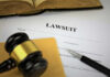 A gavel resting on a legal document titled 'LAWSUIT' with a pen and an open book in the background