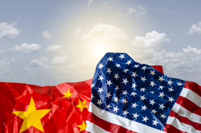 Crumpled flags of the United States and China against a cloudy sky