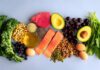 An assortment of healthy foods including fish, nuts, fruits, and vegetables arranged on a light background