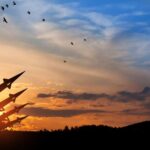 Silhouette of missiles against a colorful sunset with birds flying