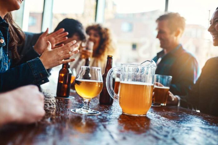 shutterstock_2478772515.jpg Group of friends enjoying drinks at a bar with a pitcher of beer on the table