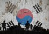 Silhouettes of soldiers in front of the South Korean flag on a cracked wall