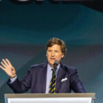 A man in a suit speaking at a podium with a microphone