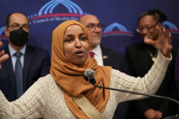 A woman in a hijab passionately speaking at a podium during a public event