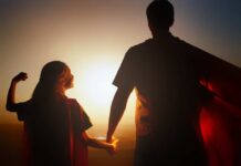 Silhouette of a parent and child wearing capes against a sunset