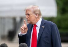 A political figure gesturing with a finger raised during a press conference