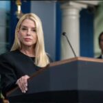 A woman at a podium during a press conference with a man in the background