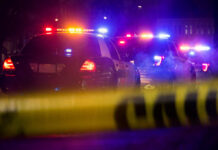 Police cars with flashing lights at a nighttime scene behind crime scene tape