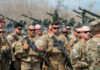 Group of military personnel in camouflage uniforms standing with weapons during a training exercise
