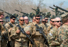 Group of military personnel in camouflage uniforms standing with weapons during a training exercise