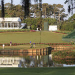 A scenic view of a golf course with players and maintenance equipment near a water feature
