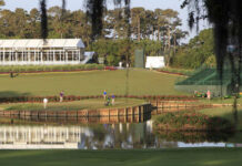 A scenic view of a golf course with players and maintenance equipment near a water feature