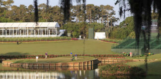 A scenic view of a golf course with players and maintenance equipment near a water feature