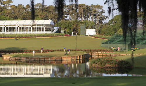 A scenic view of a golf course with players and maintenance equipment near a water feature