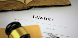 A gavel resting on a legal document titled 'LAWSUIT' with a pen and an open book in the background