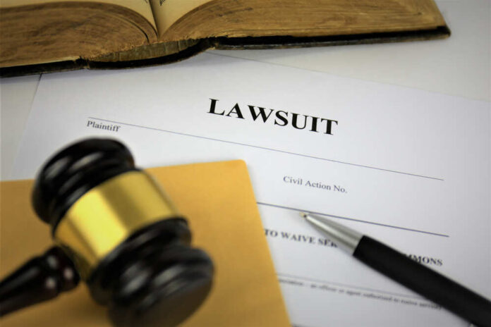 shutterstock_1236208948.jpg A gavel resting on a legal document titled 'LAWSUIT' with a pen and an open book in the background