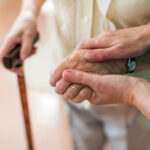 Federal Betrayal: Retirees Forced into Labor Two hands clasped together, one elderly and one younger, with a cane in the background