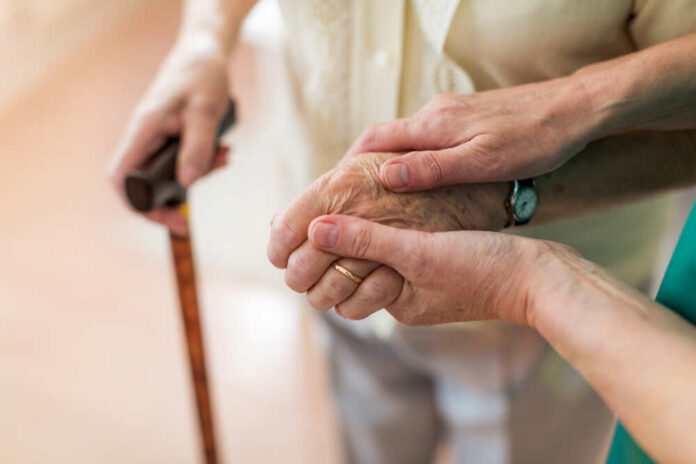 shutterstock_1382745380.jpg Two hands clasped together, one elderly and one younger, with a cane in the background