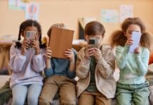 Four children sitting together, each focused on their electronic devices